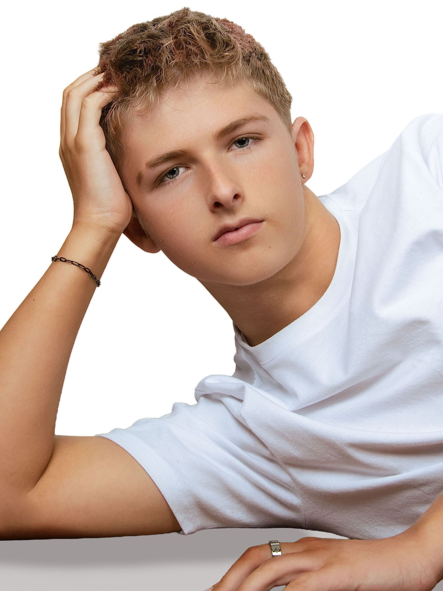 Young man in white t-shirt with bracelet and ring, hand in hair, posing against white background.