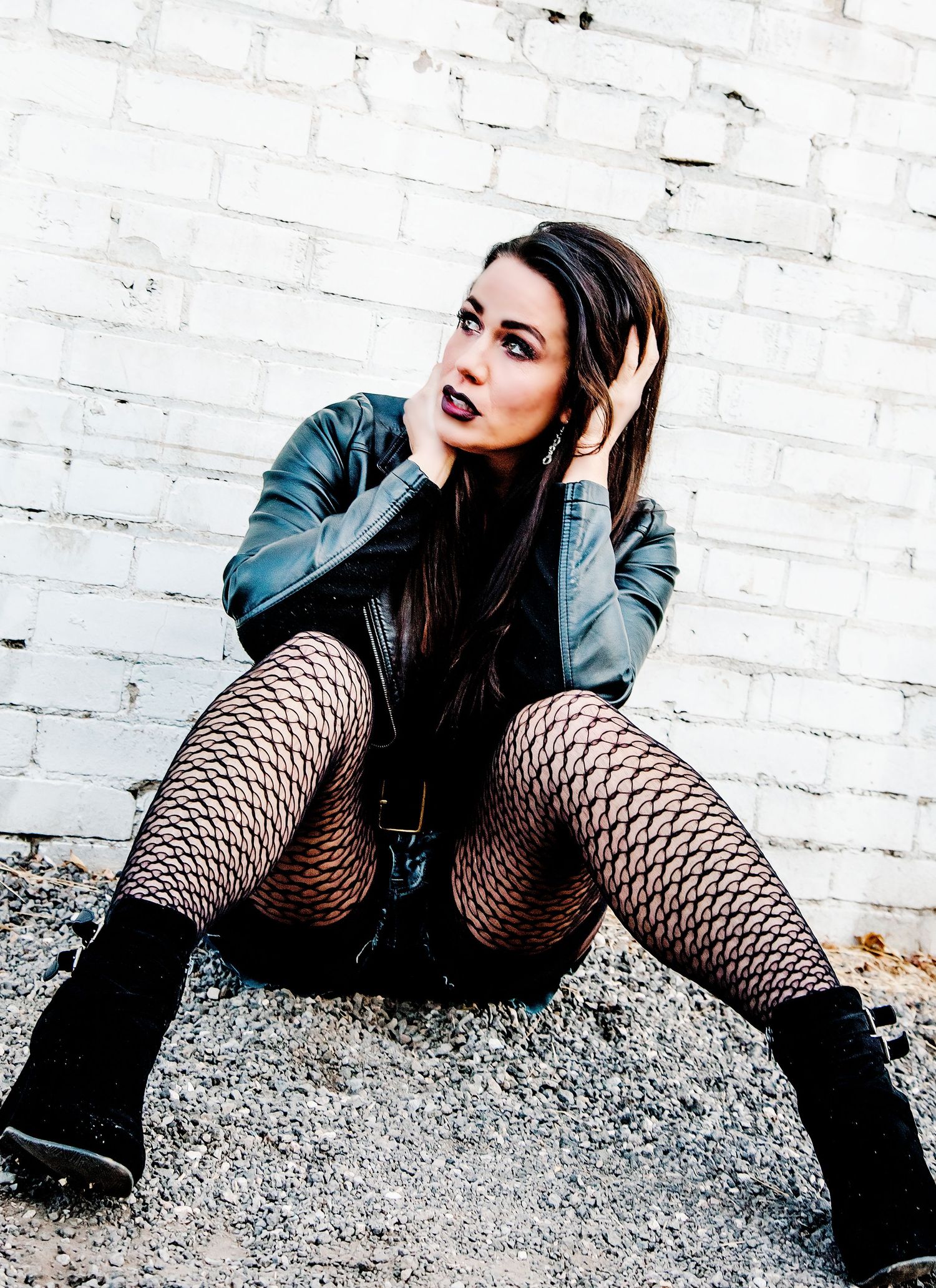 Urban fashion portrait against white brick wall featuring leather and fishnets.