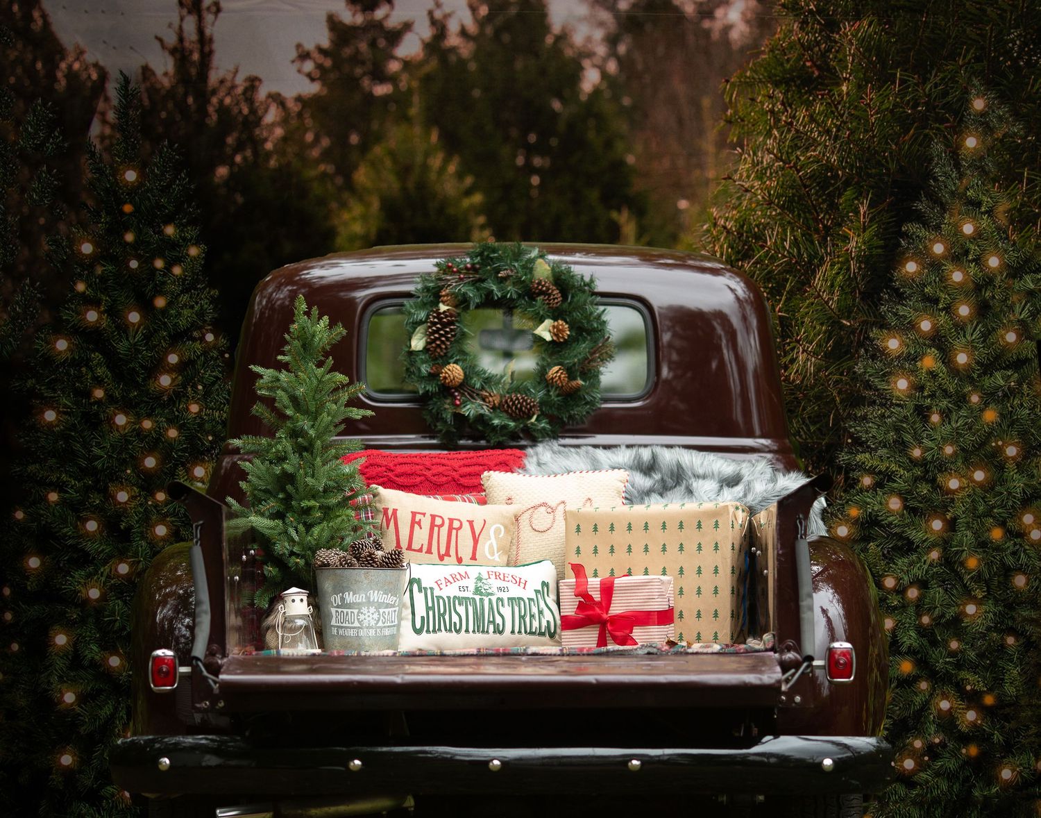 A red vintage pickup truck decorated with Christmas trees and lights sits in front of a festive holiday display.