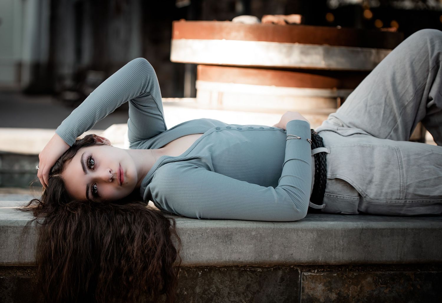 Dramatic portrait of someone in light blue lying on concrete steps at sunset.