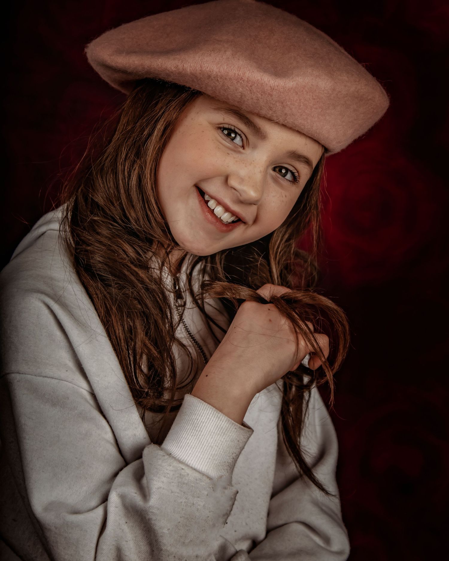 Portrait in a brown beret and grey sweater against deep red background.