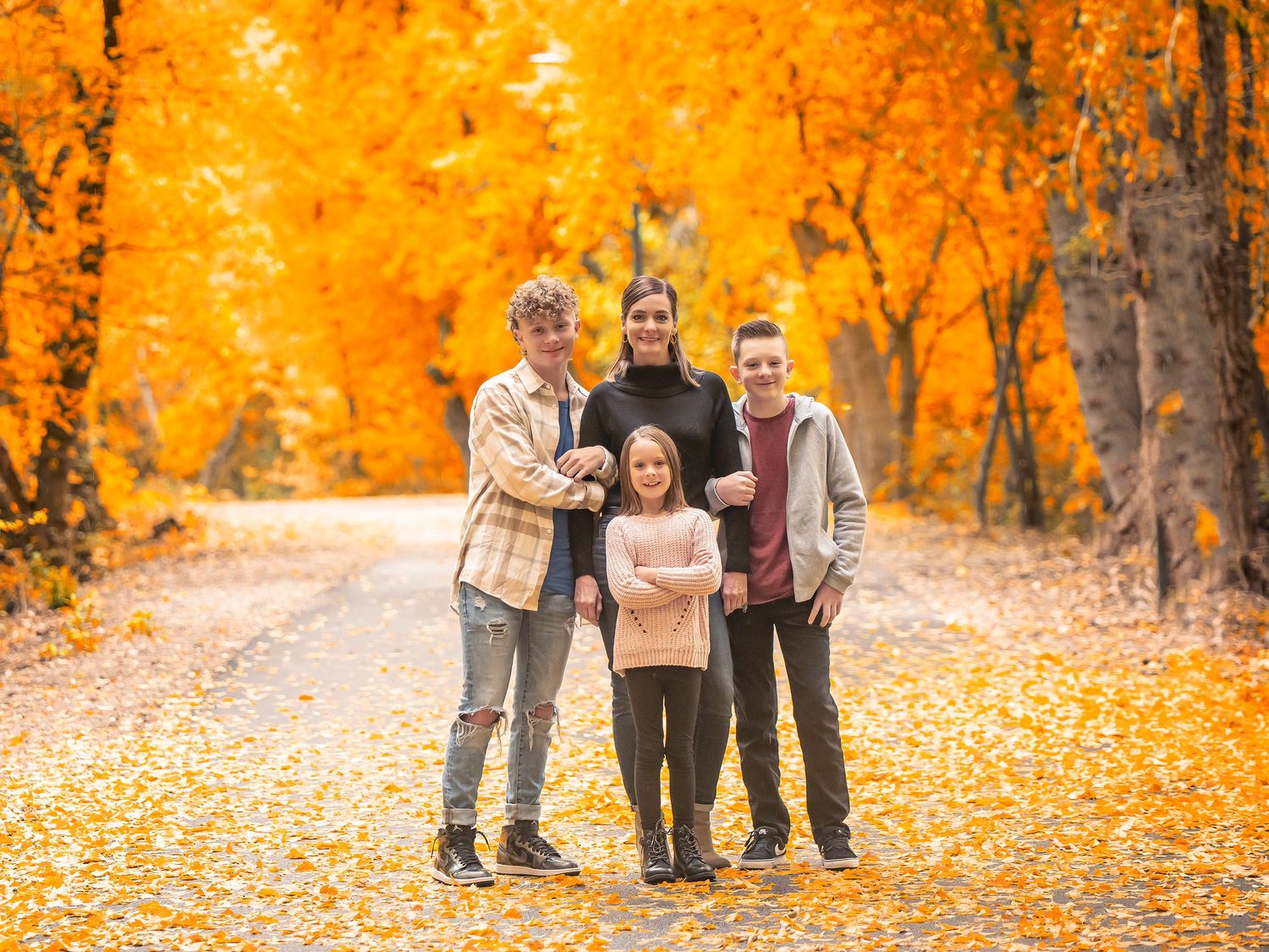 Family standing together on autumn path covered in vibrant golden leaves and fall foliage.