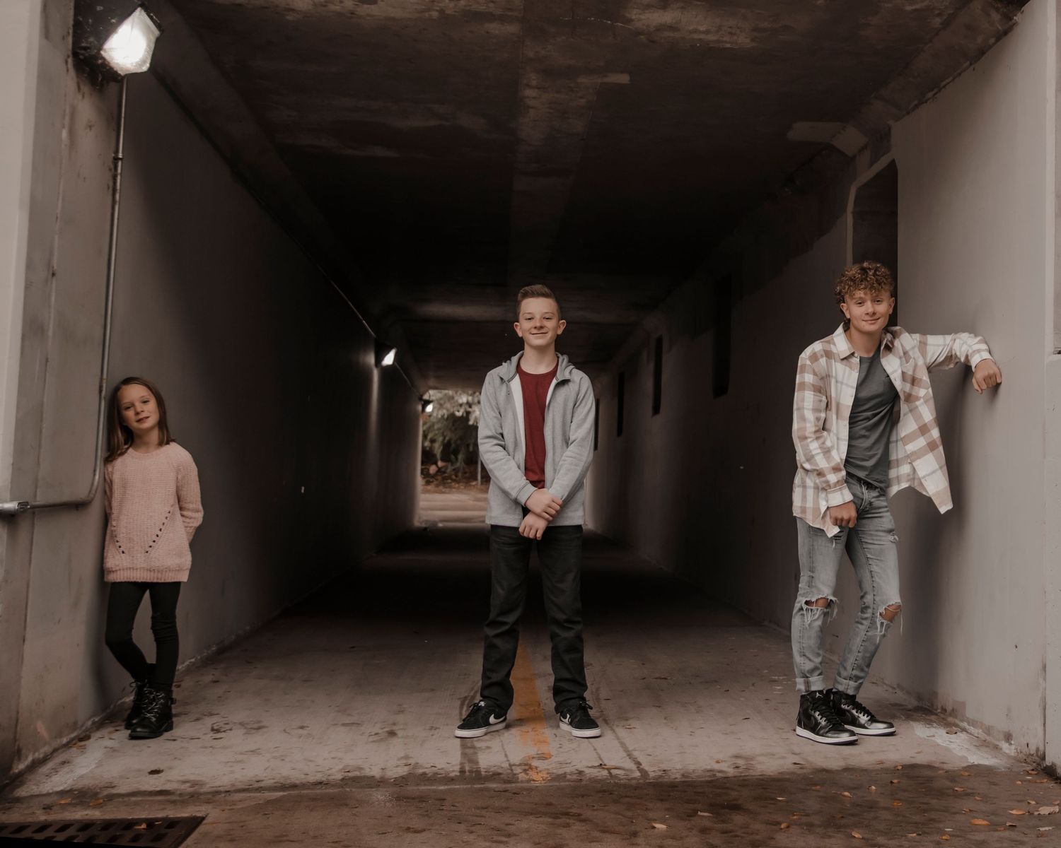 Three subjects posing in an urban concrete tunnel with dramatic lighting.