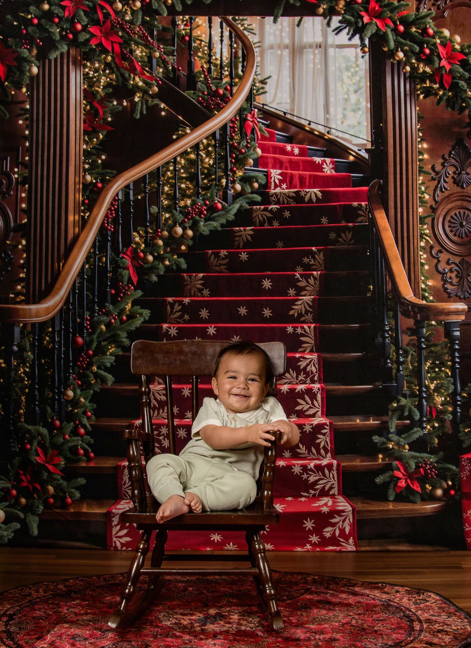 Elegant Christmas staircase decorated with red ribbons and greenery, featuring a small rocking chair on an ornate rug.