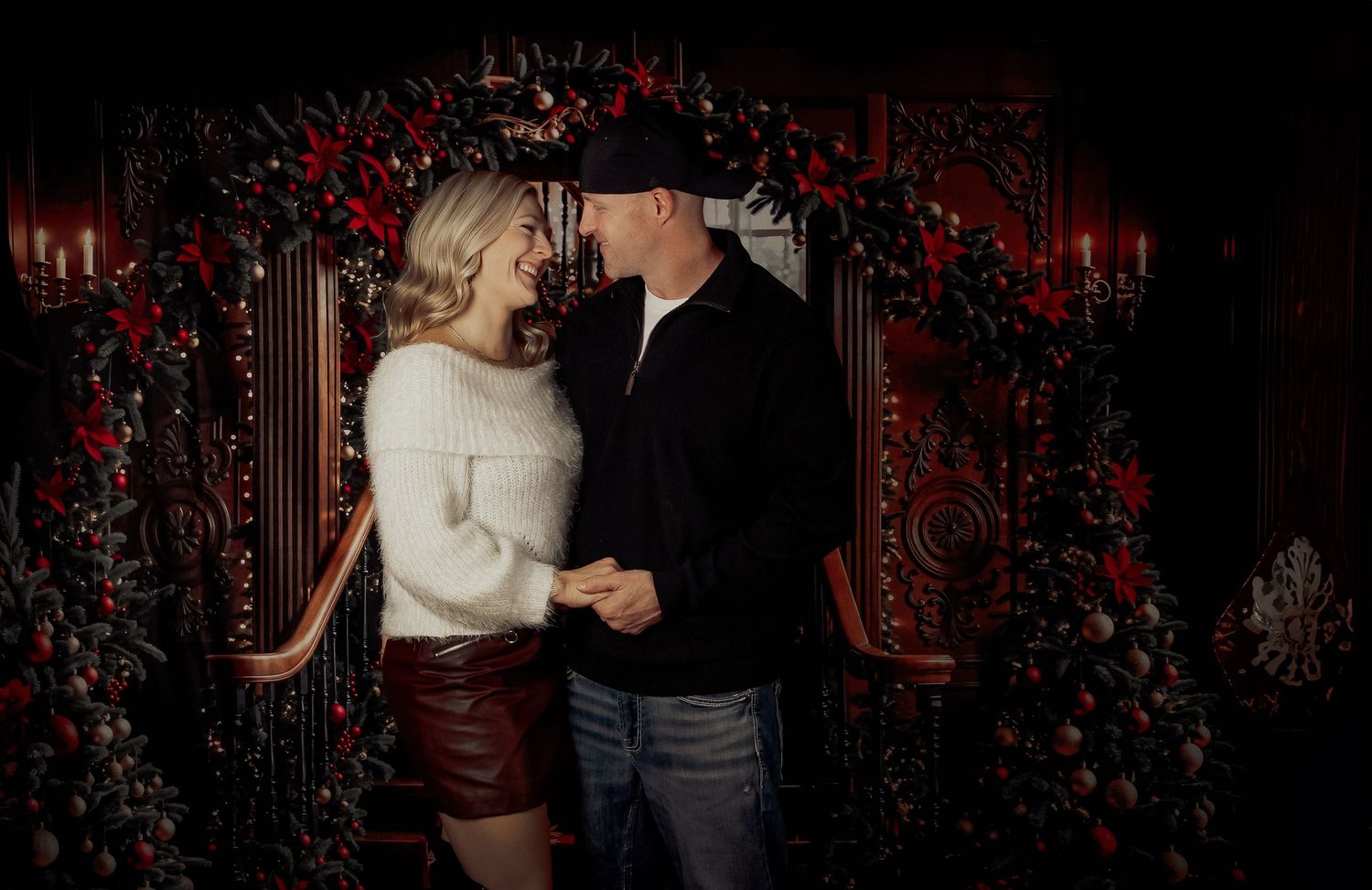 A romantic couple dances together in front of a backdrop decorated with deep red roses and elegant lighting.
