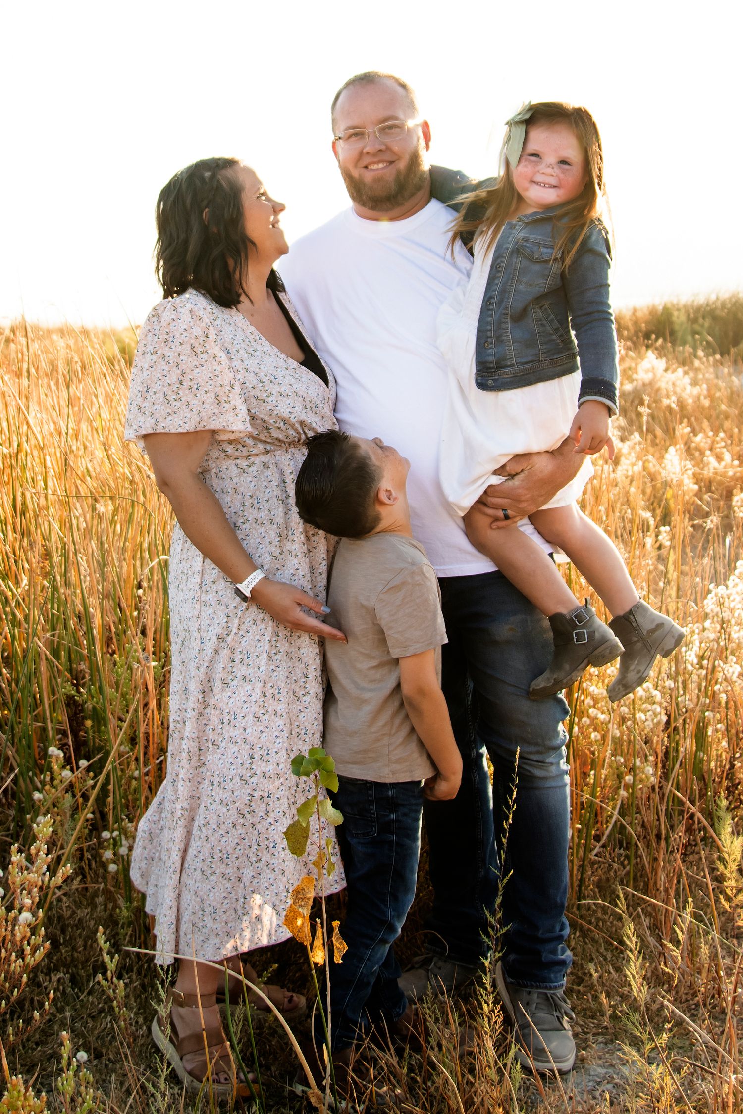 Family standing together in tall grass field during sunset in casual attire.