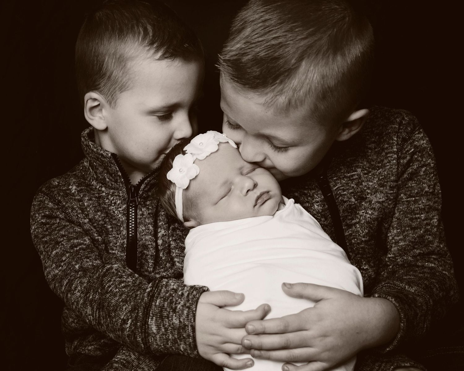 Black and white portrait of siblings sharing tender moment with newborn.
