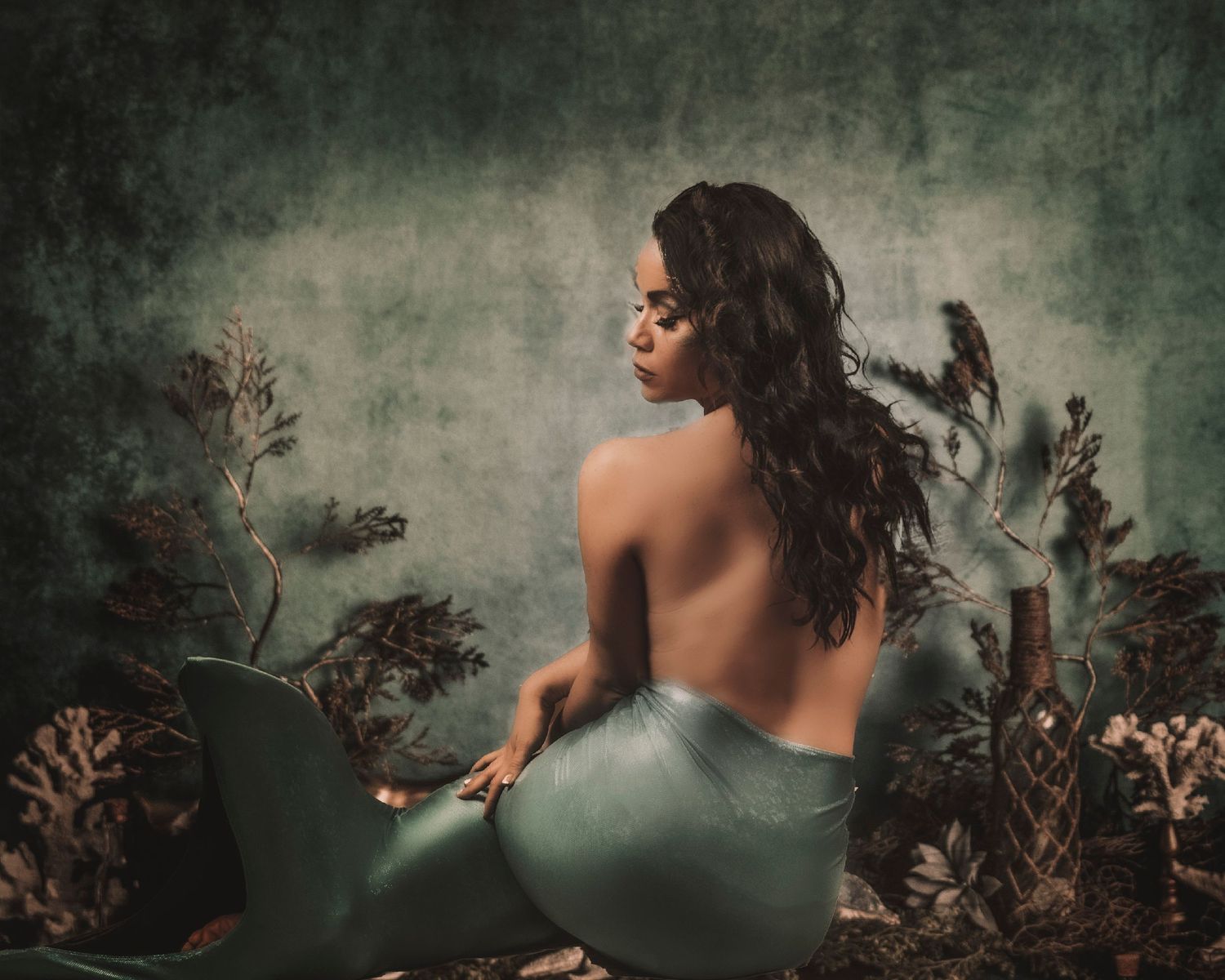 Artistic portrait in teal dress against mystical nature backdrop.