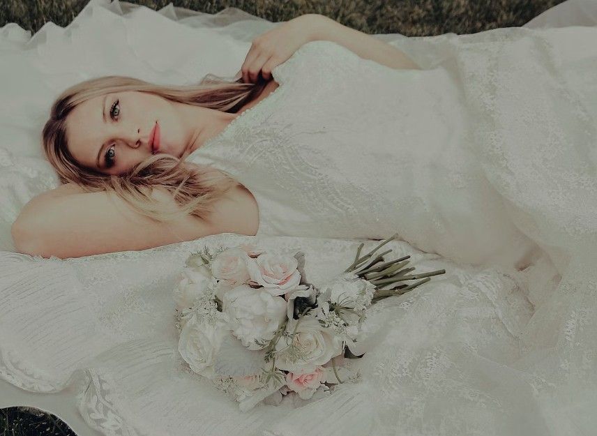A dreamy wedding portrait of someone lying on white fabric with delicate flowers and artistic composition.