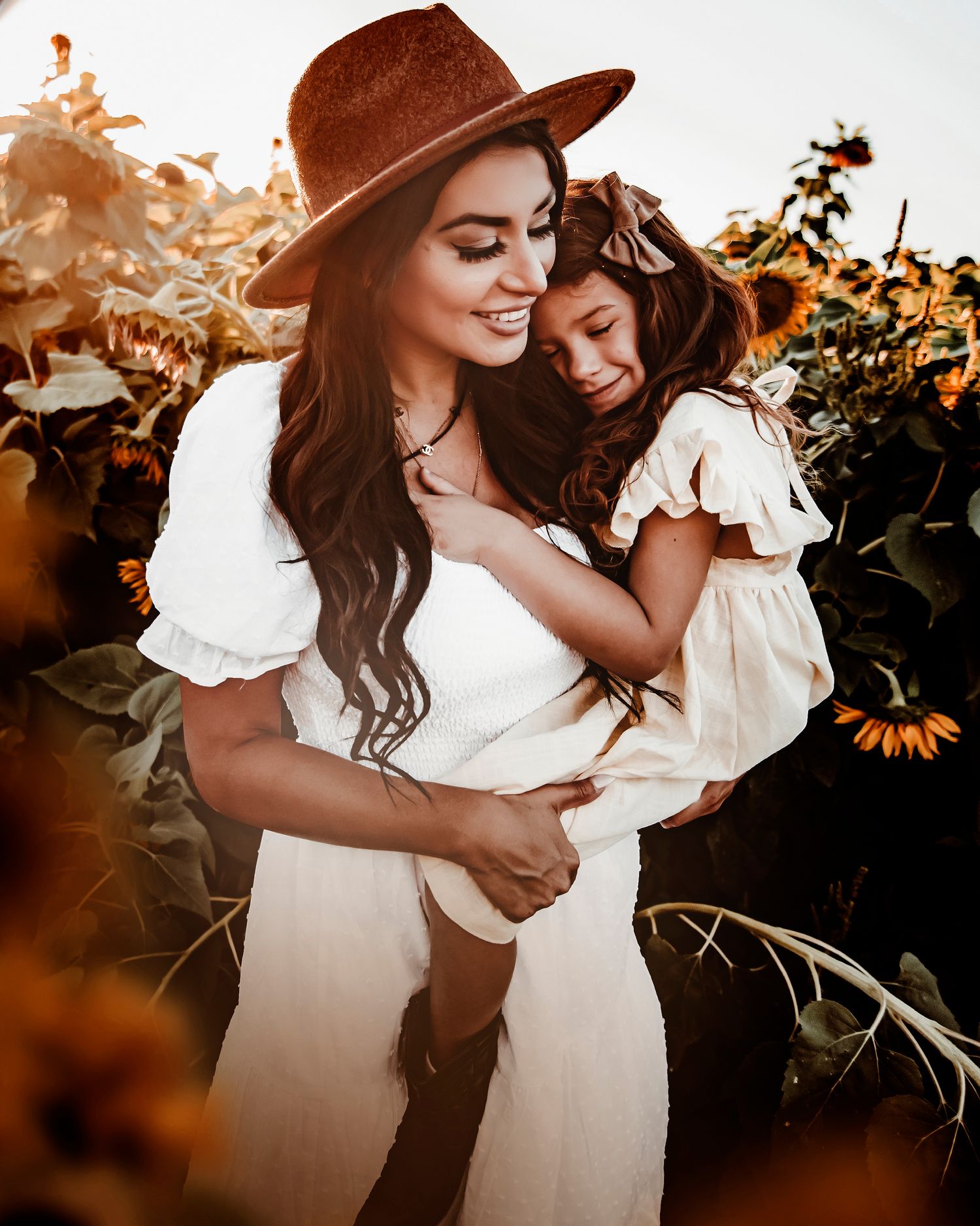 A tender moment captured in a sunflower field at sunset with warm golden light and flowing white dresses.