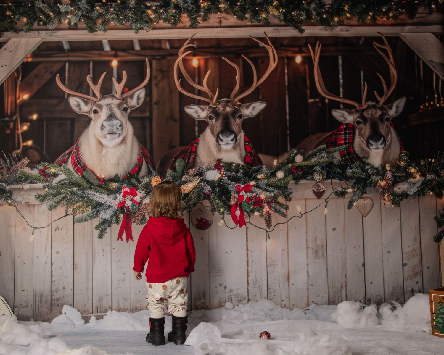 Rustic wooden wall decorated with deer antlers, red Christmas stockings, and twinkling holiday lights creating a cozy scene.