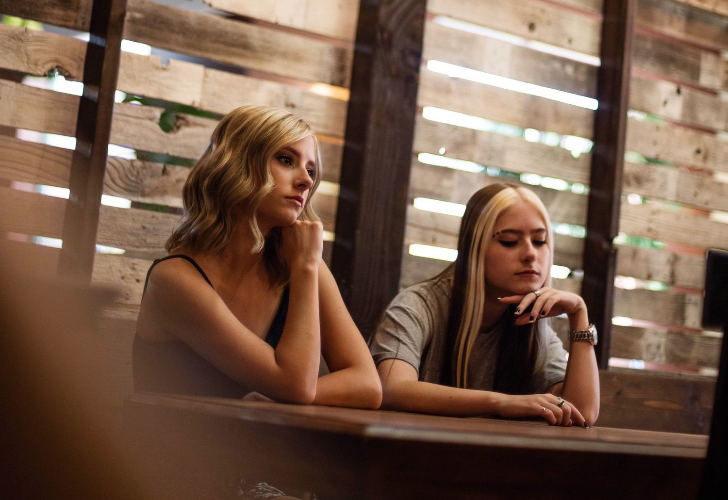 Two friends resting with thoughtful expressions at a rustic wooden table in warm lighting.