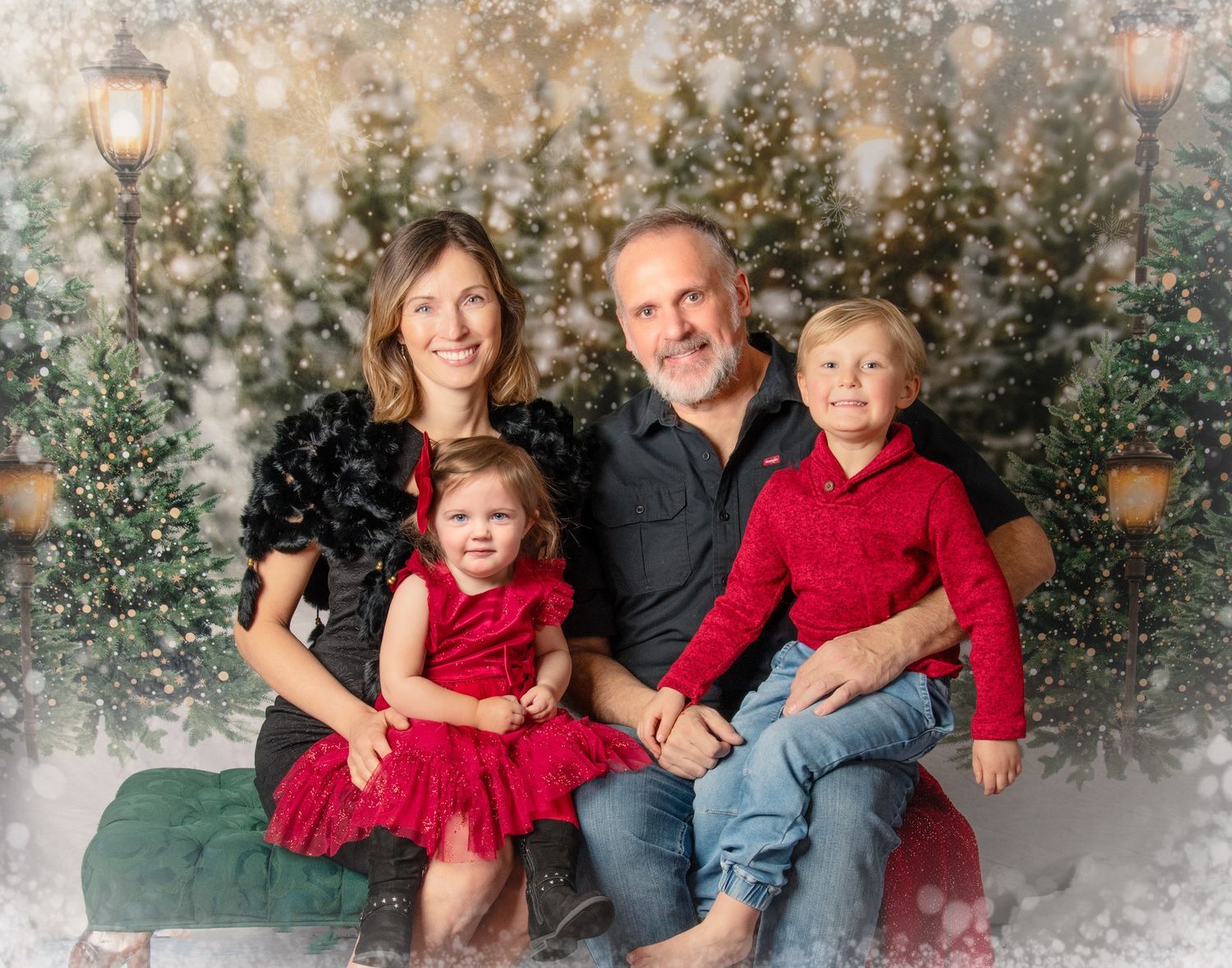 A family wearing coordinating red and gray outfits poses for holiday portraits in front of a snowy winter backdrop.