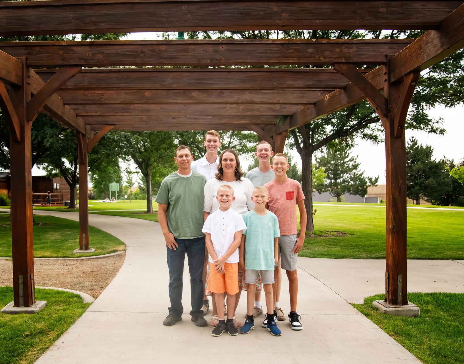 Group portrait under a wooden pergola in a park setting on a sunny day.