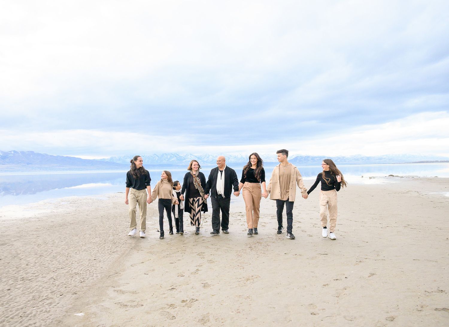 Group walking together along a scenic beach with mountains and cloudy skies in the background.