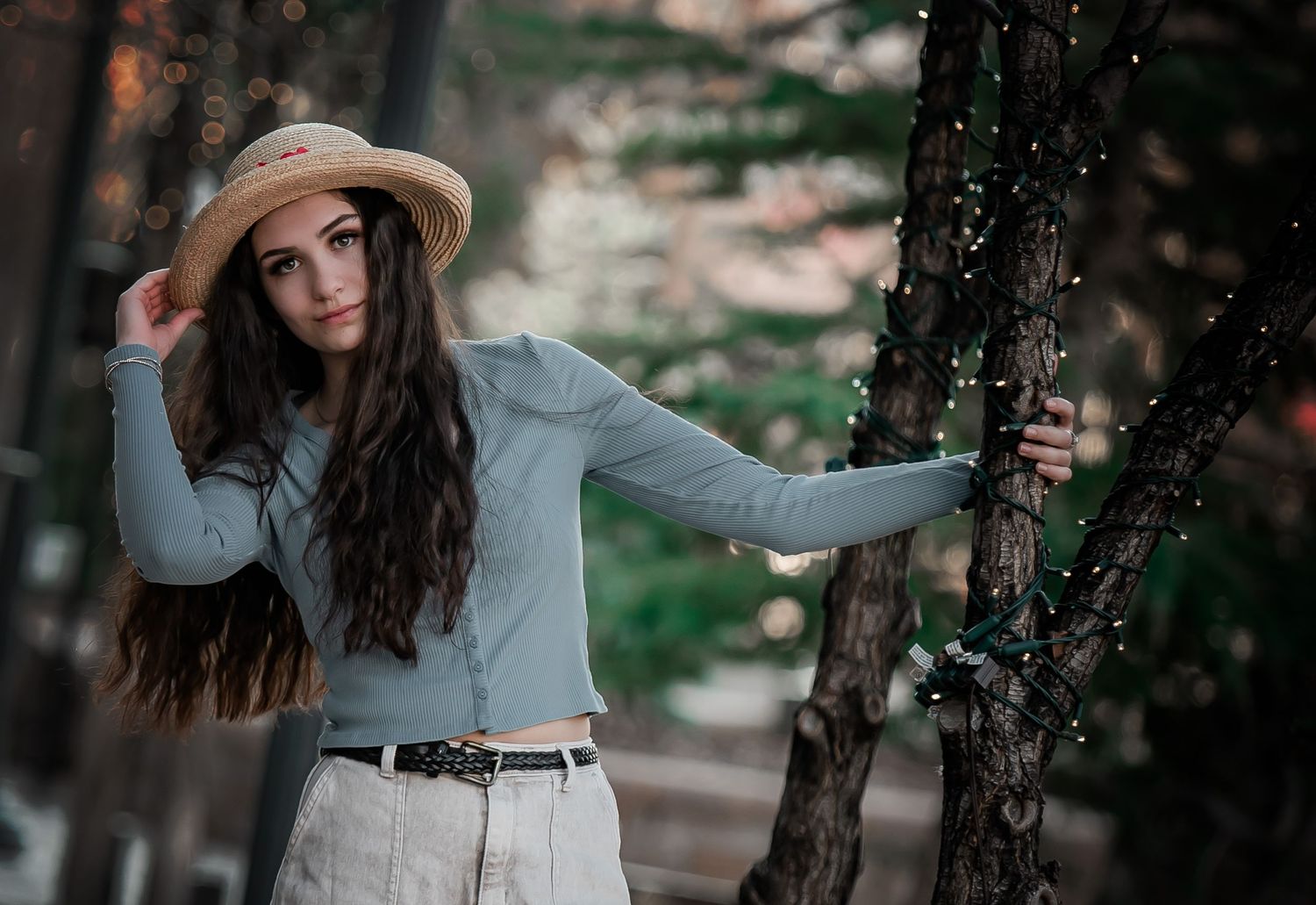 Someone in a beige hat and blue sweater poses playfully near trees in a natural outdoor setting.