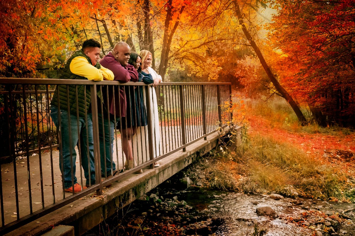 Group leaning on metal railing of bridge pathway surrounded by bright fall colors.