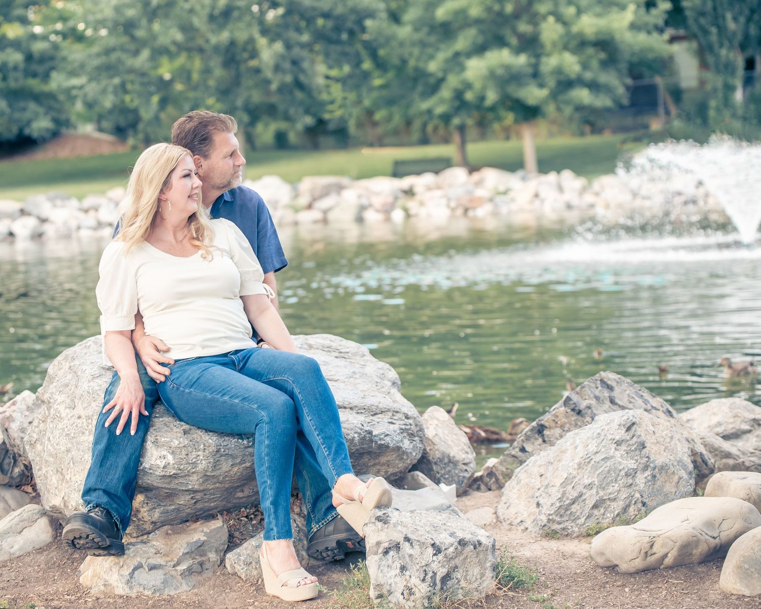 Couple sits together on rocky shoreline overlooking peaceful lake.