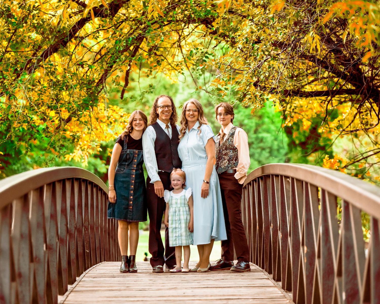 Group standing together on wooden bridge surrounded by bright yellow autumn foliage.