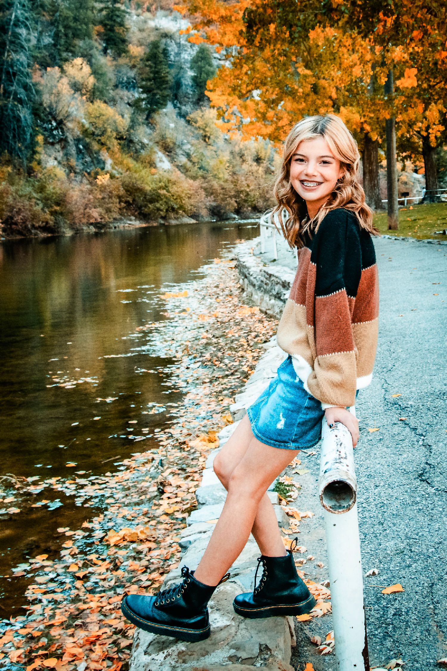 Person stands by a river during autumn with colorful fall foliage reflecting in the water on a path.