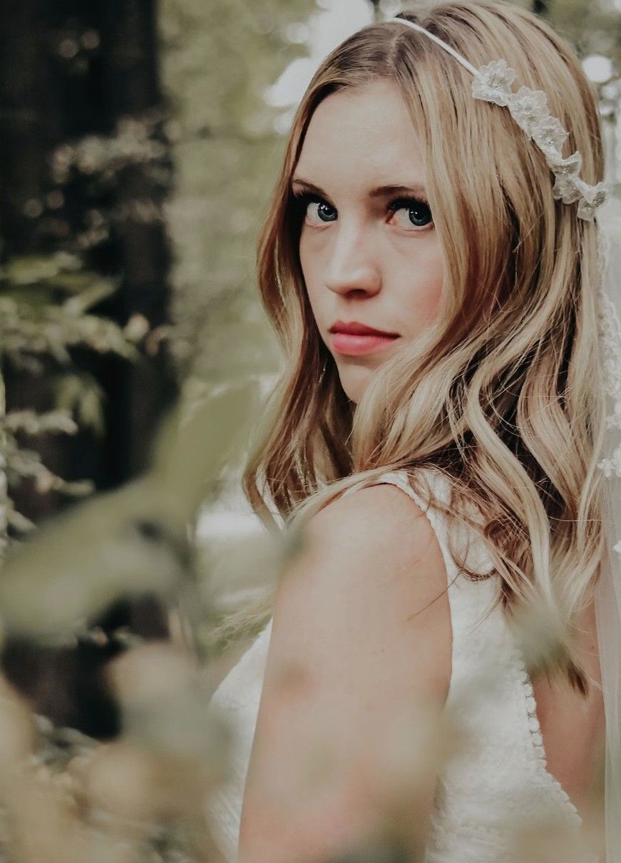 A portrait in a woodsy setting shows a delicate lace headpiece and blonde waves against a soft green background.