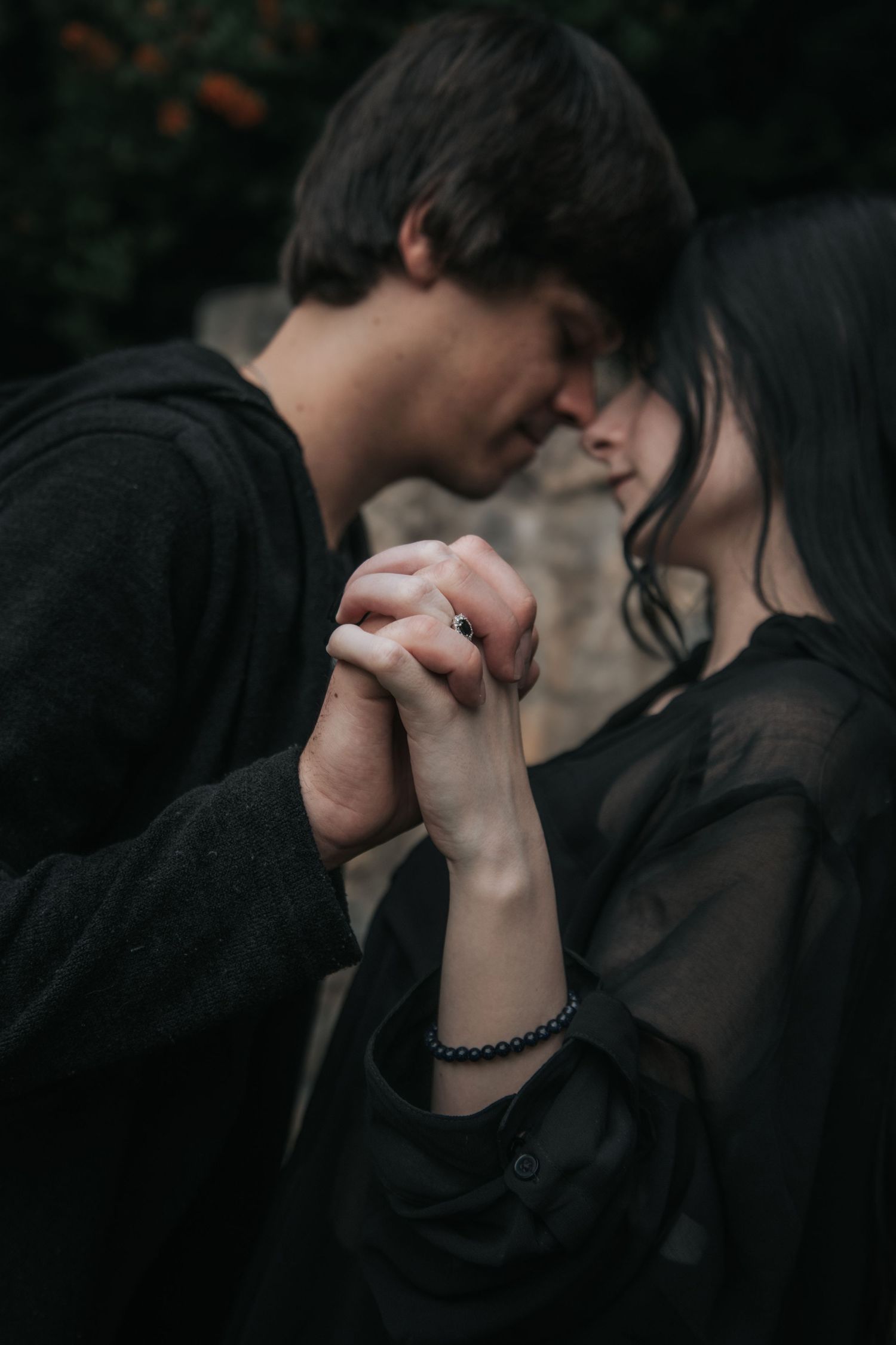 Artistic portrait of couple in dark clothing sharing tender moments in a dimly lit setting.