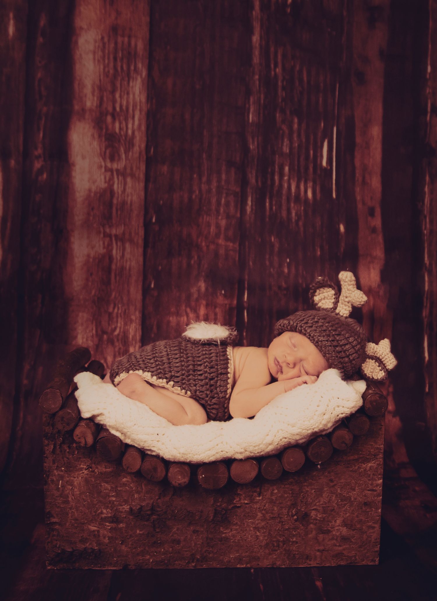 Rustic newborn photo with knit bear outfit on wooden backdrop.