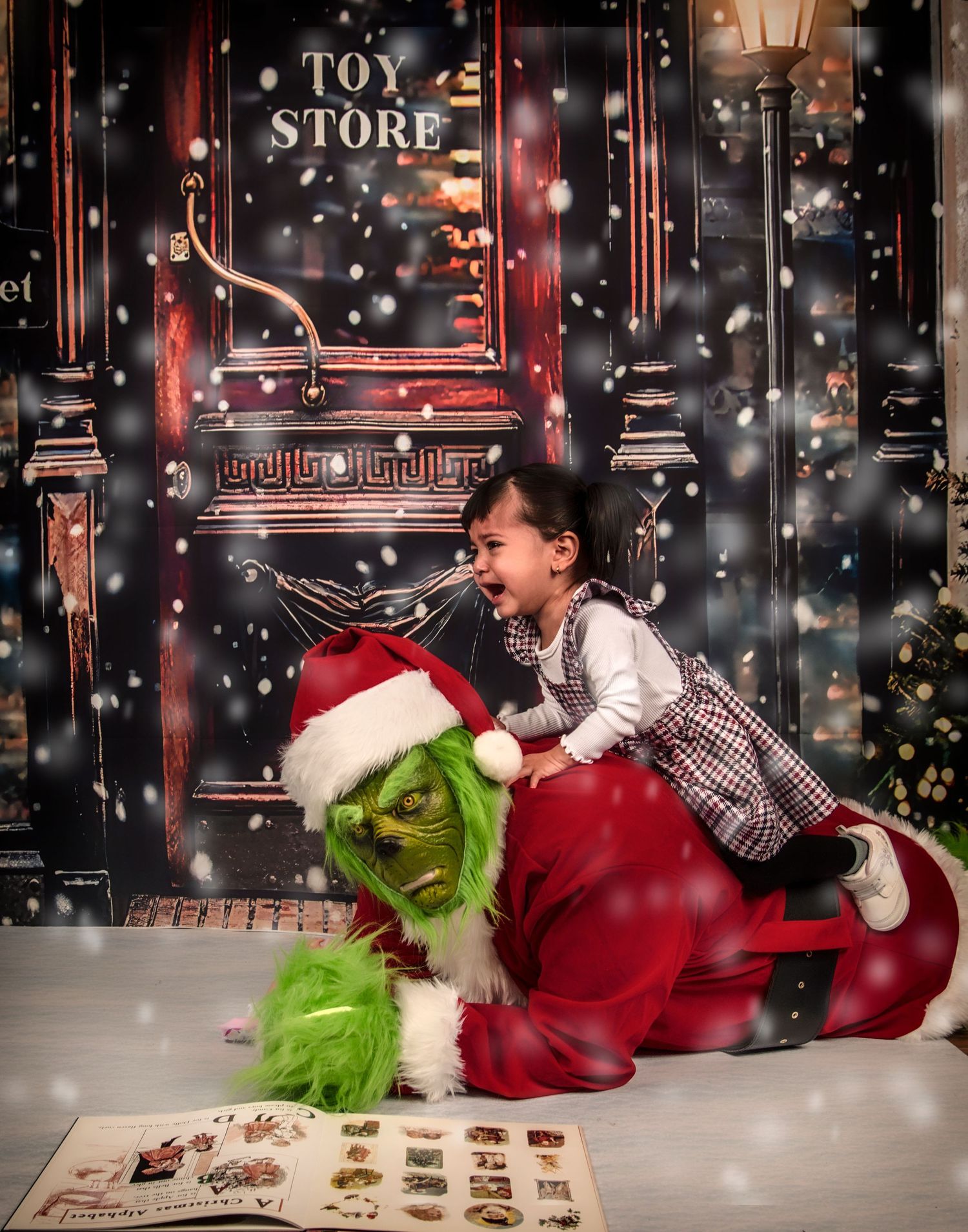 A festive holiday scene with a green Grinch character in Santa attire looking at a book while snow falls outside a store window.
