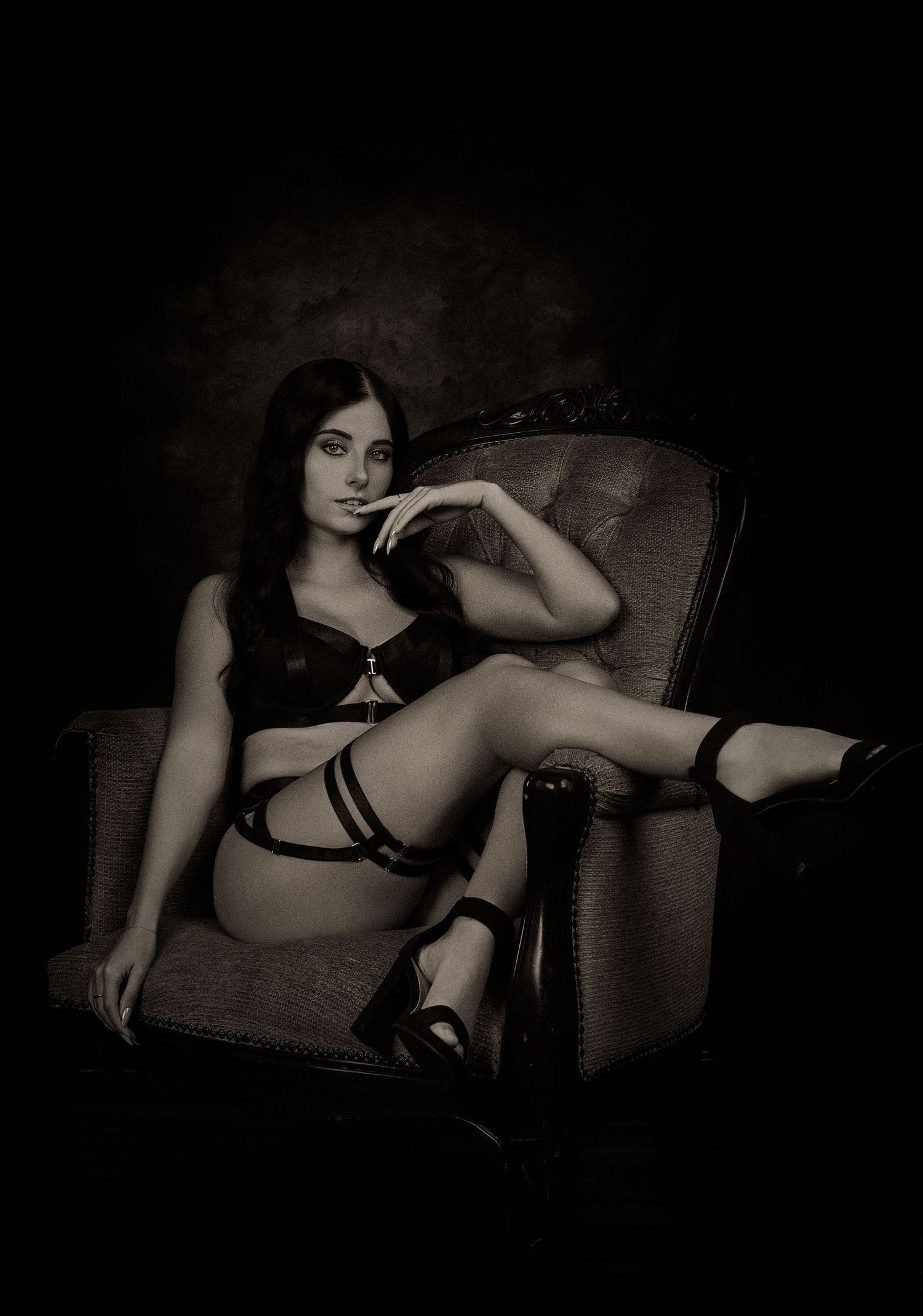 Black and white portrait of woman in lingerie seated in vintage armchair.