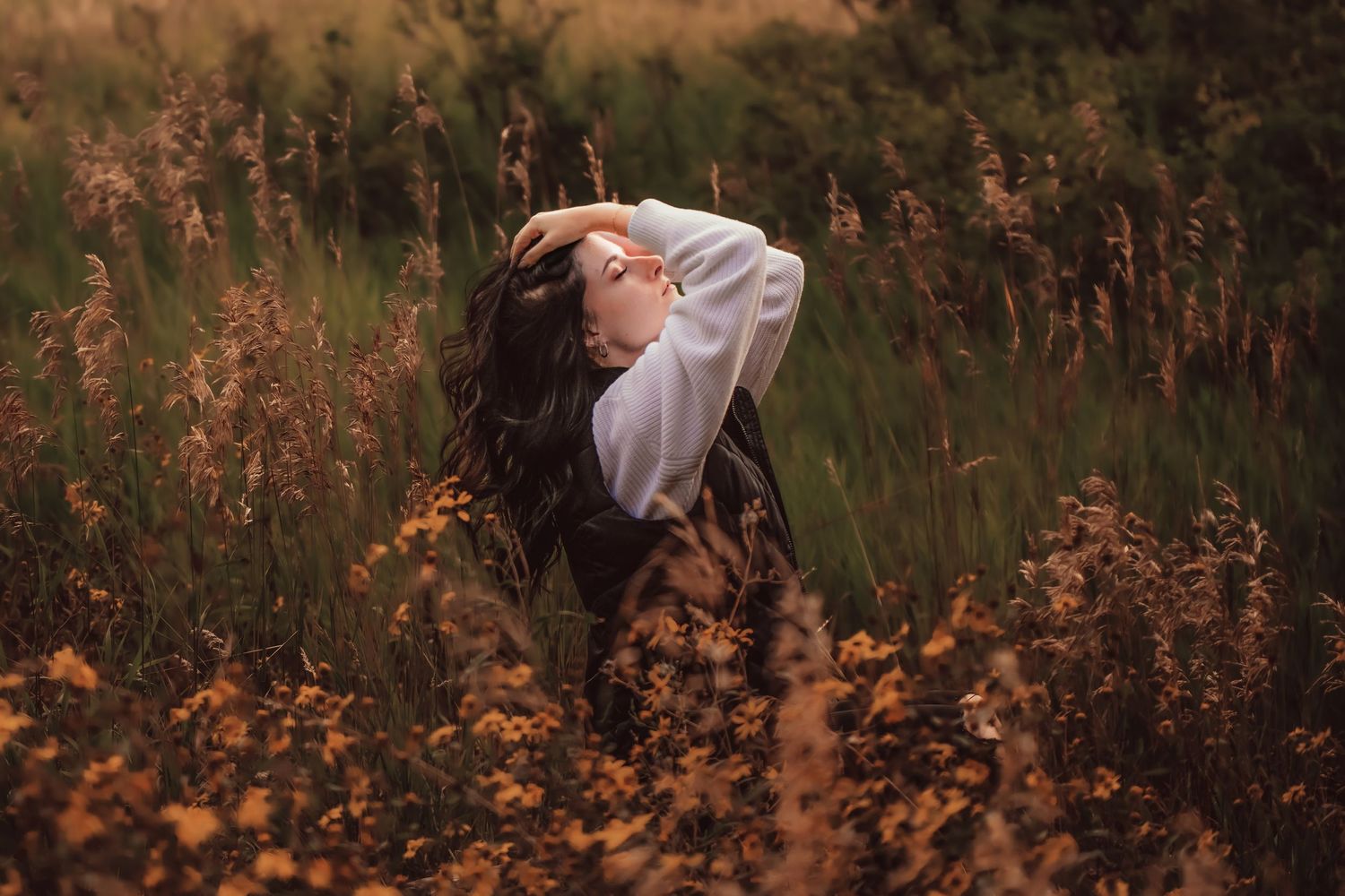 Artistic portrait of a person in a field with golden wildflowers looking skyward at sunset.