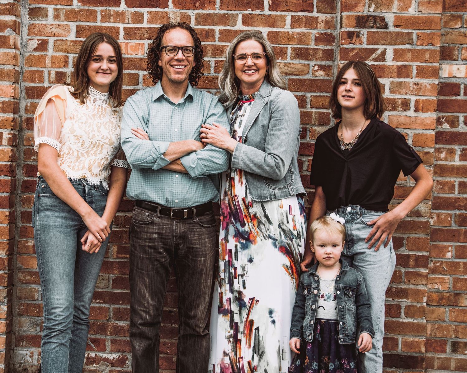 A casual family group portrait against a rustic brick wall background.