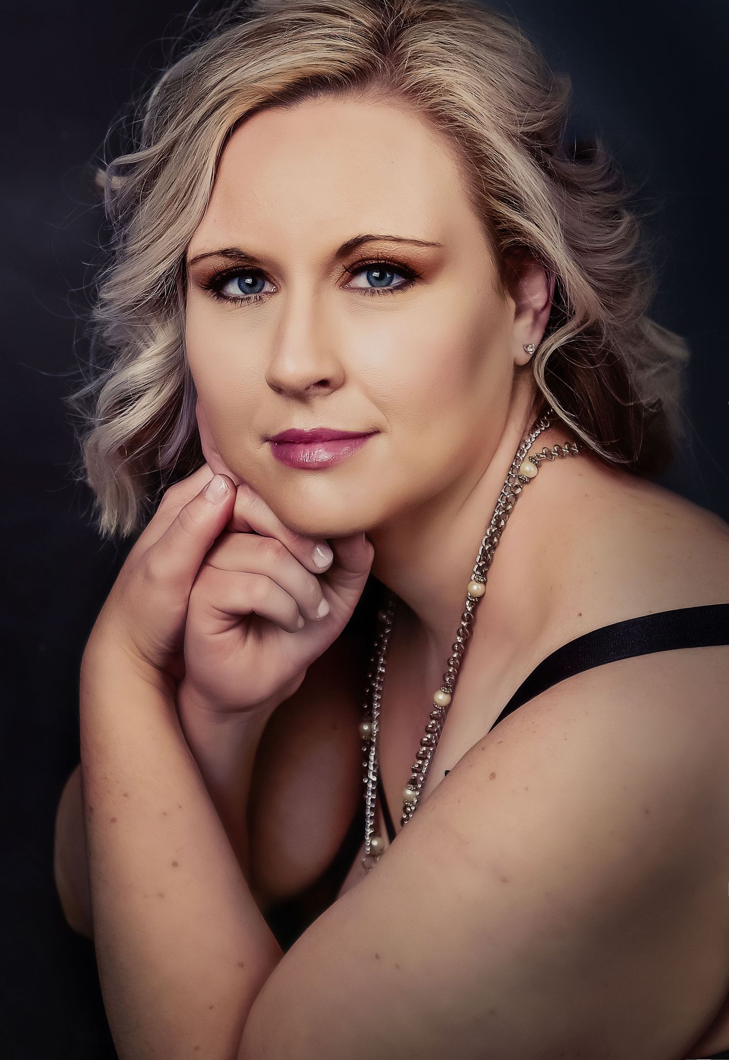 Professional glamour portrait of a woman with silver hair wearing a black dress and jewelry.