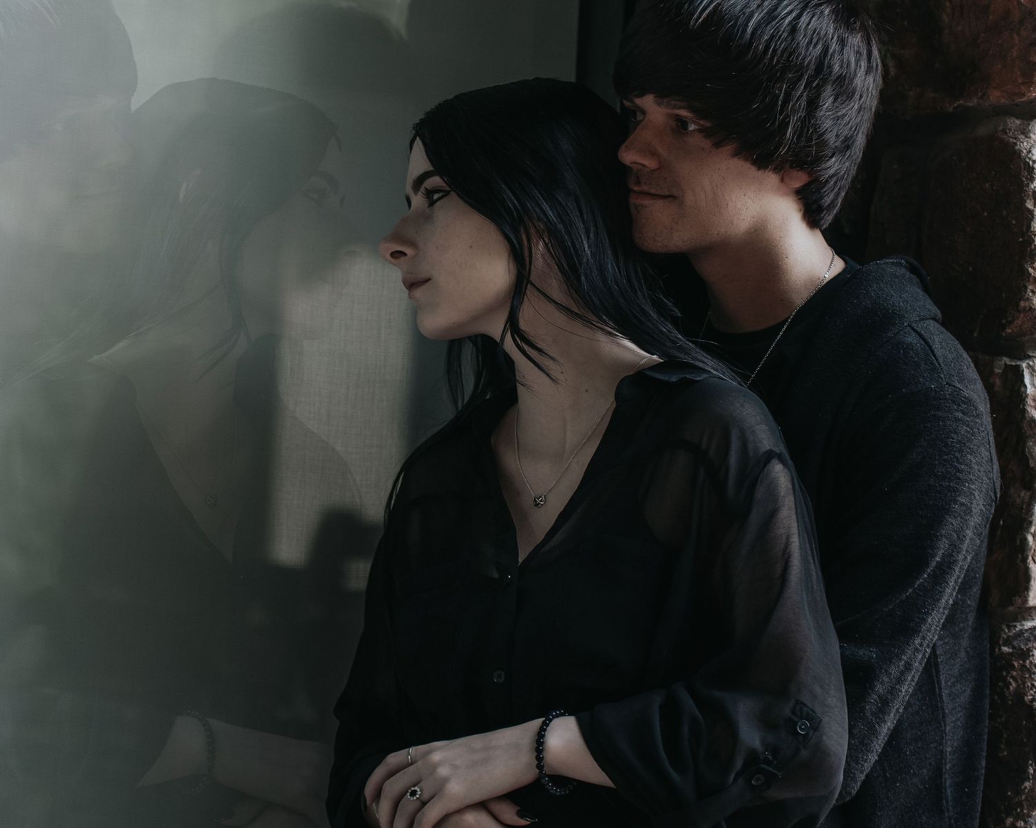 Intimate couple poses together against dark background in artistic black and white portrait series.