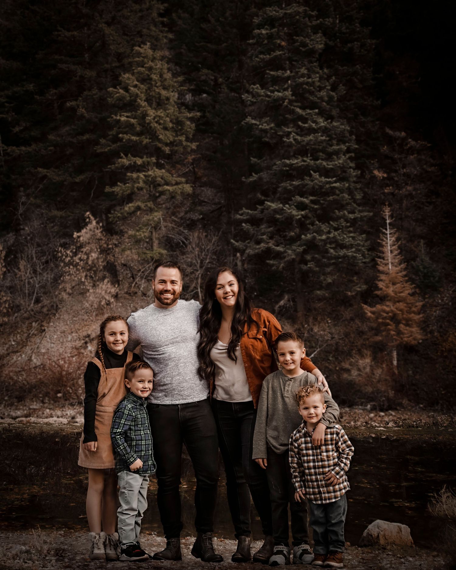 A family portrait of six people standing together against a dark forest backdrop.