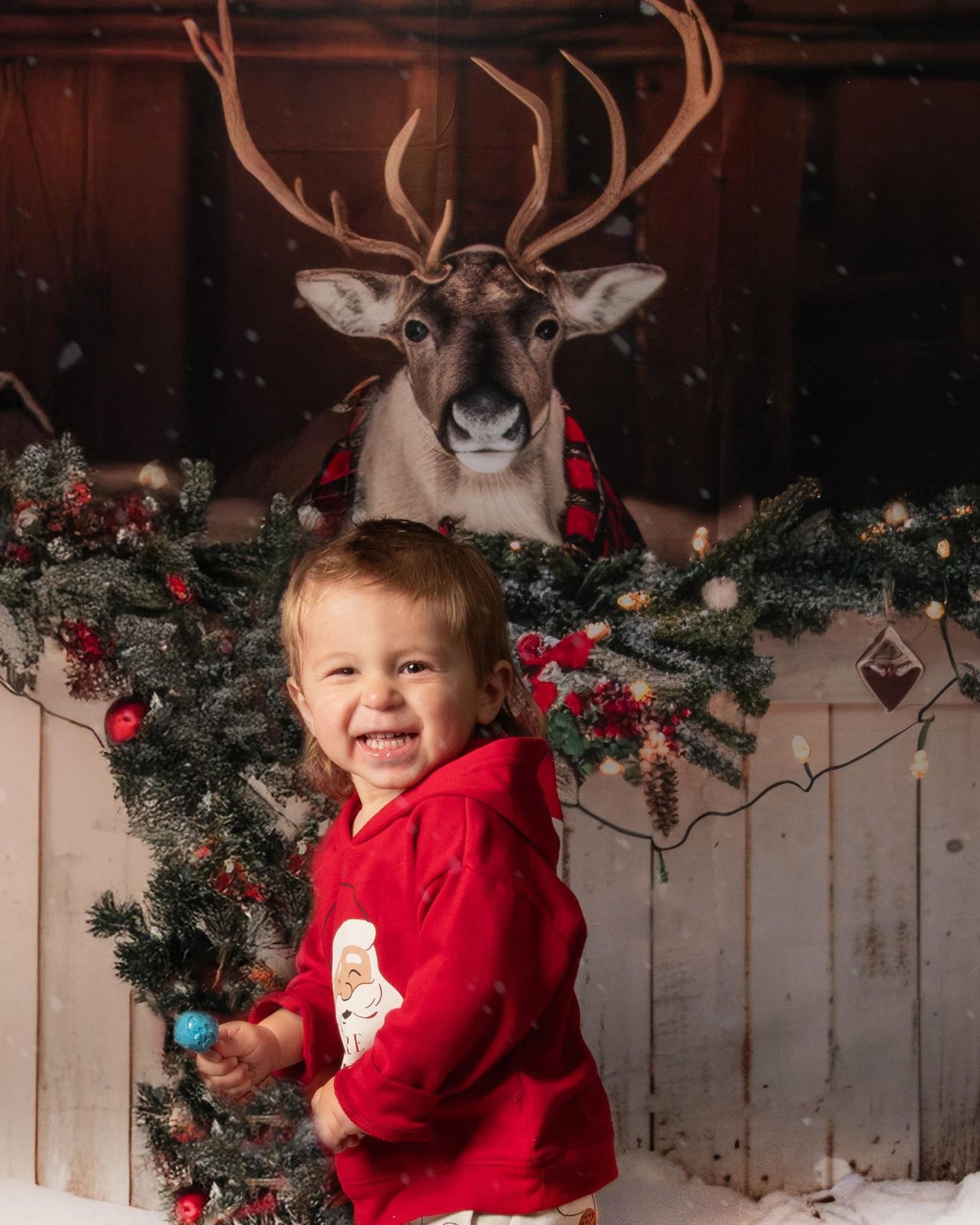 A festive holiday scene with red clothing against a rustic wooden backdrop decorated with evergreen garland and ornaments.