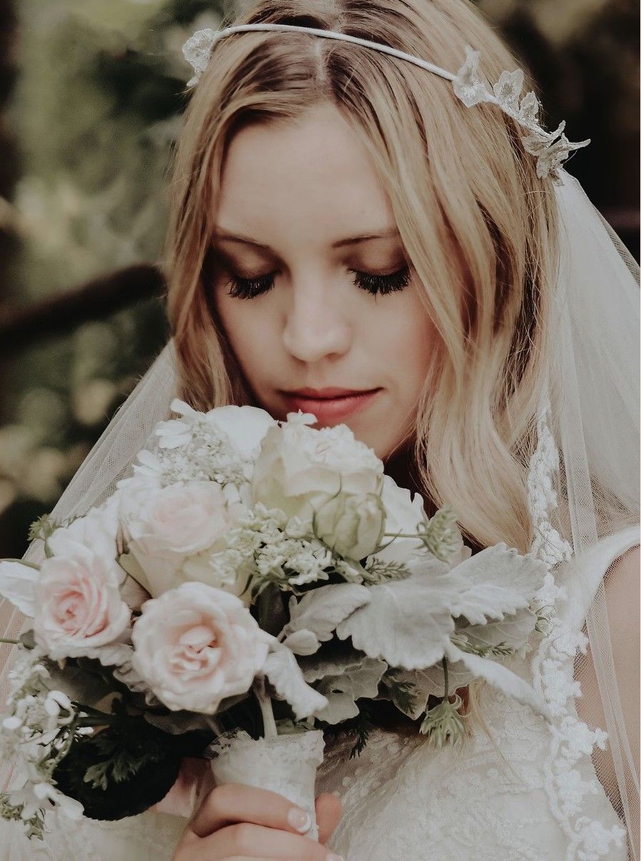 Romantic wedding portrait of bride holding blush pink and white rose bouquet with delicate lace veil and floral headpiece.