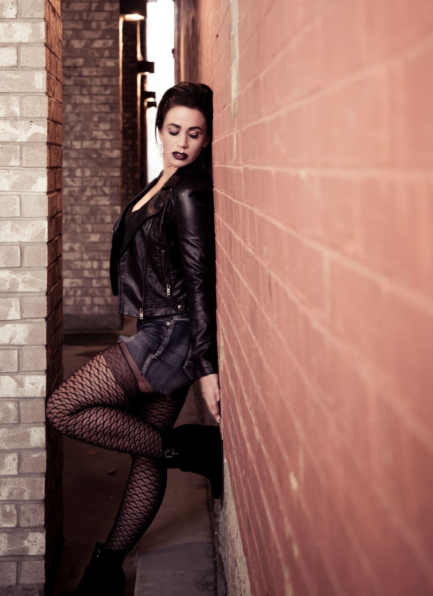 Moody fashion portrait in an alley featuring leather jacket and dramatic lighting.