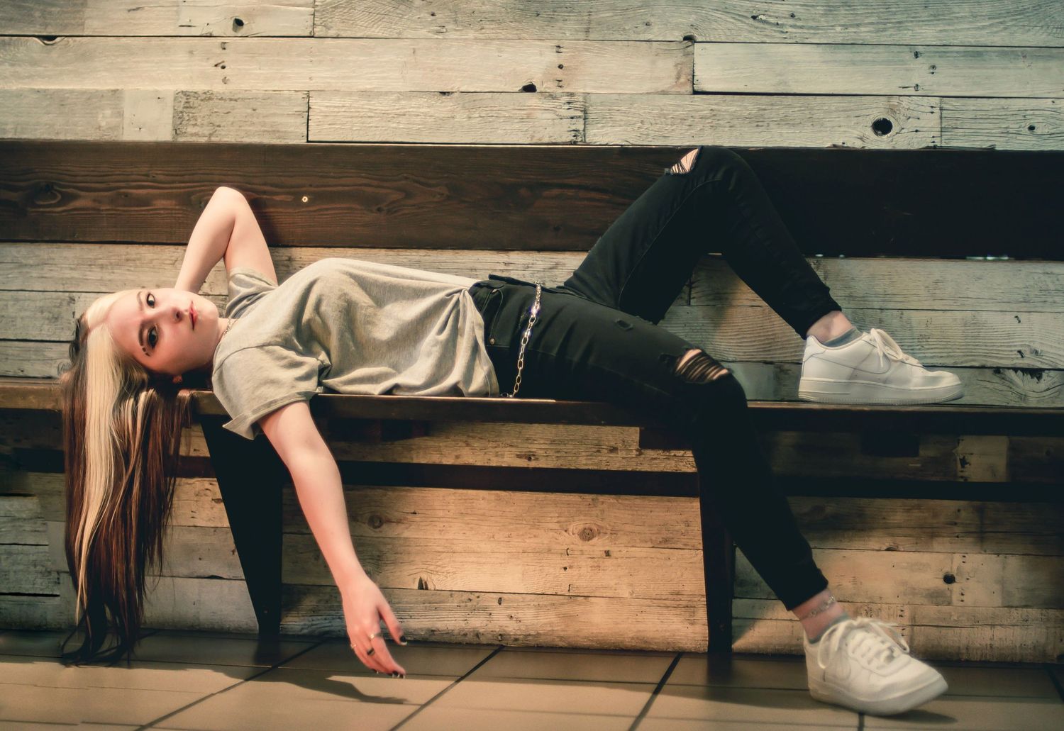 Person lying dramatically on wooden bleachers in casual attire.