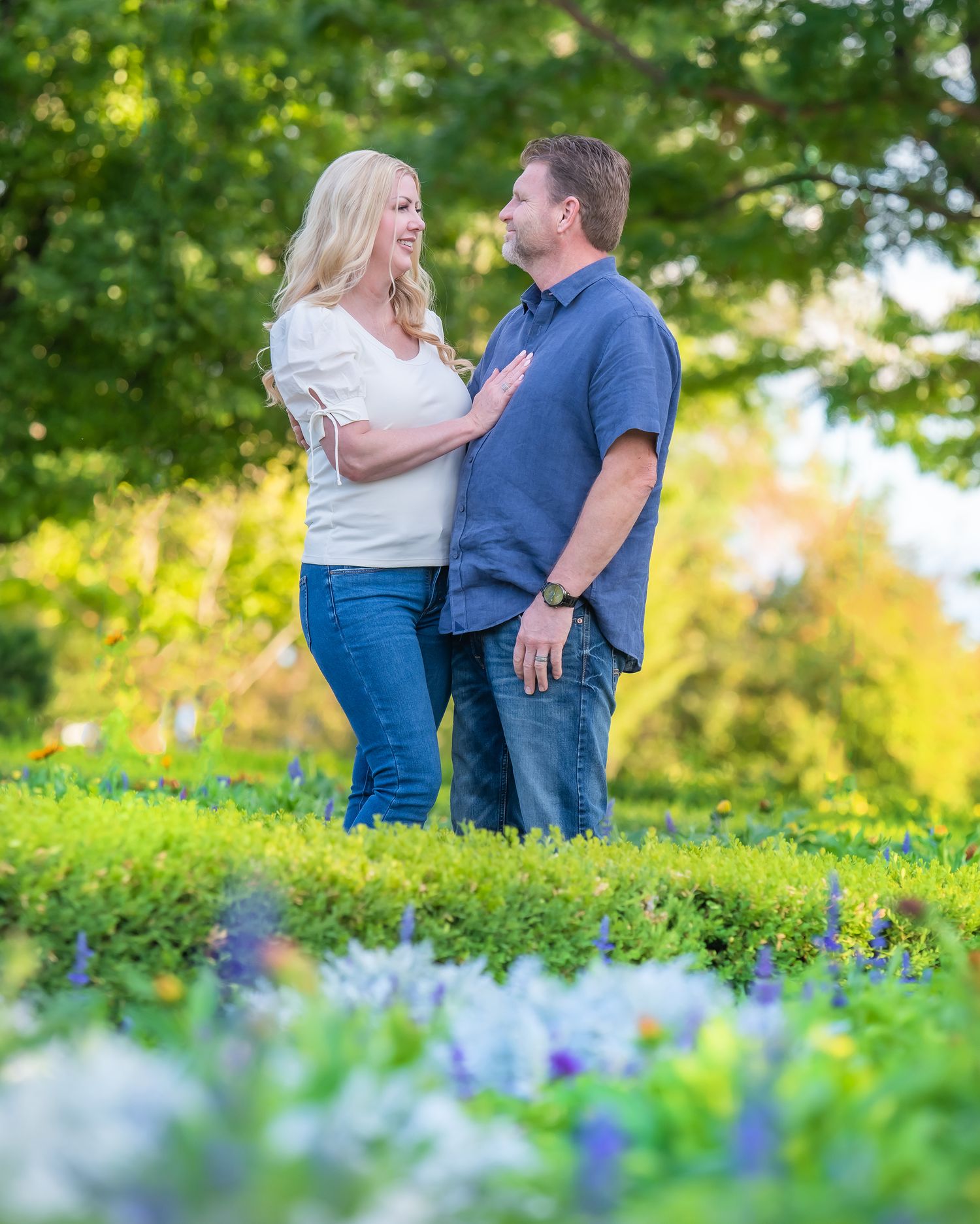 Couple stands together in garden with blooming blue flowers in foreground.