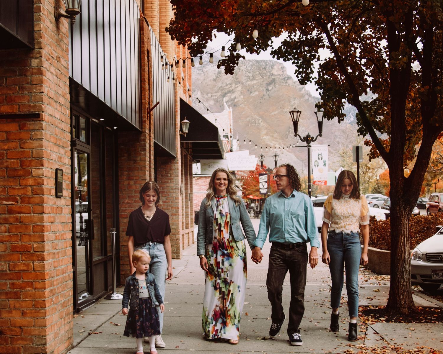 A small group walks casually down a brick-lined sidewalk on an autumn day in a downtown setting.