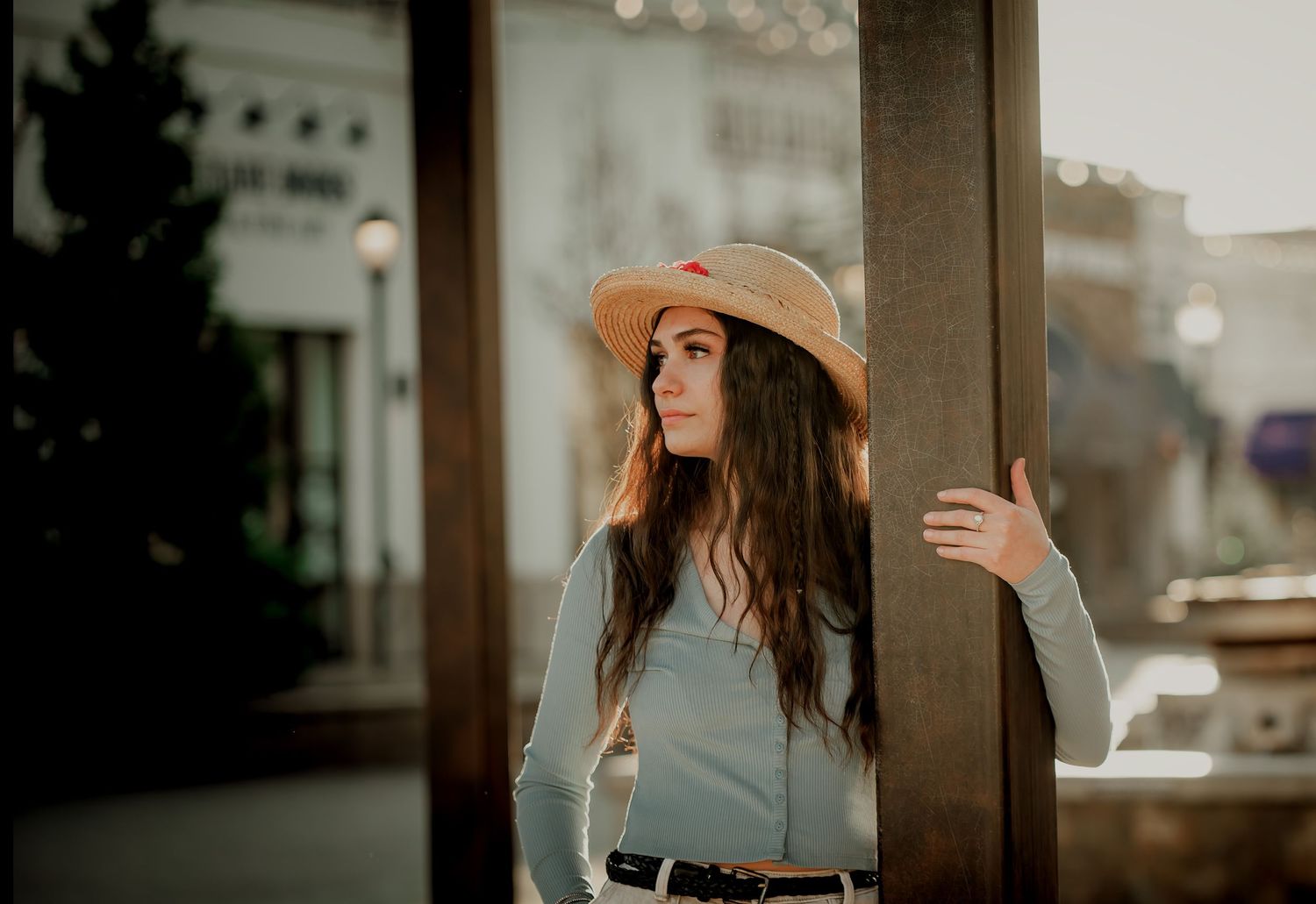 Artistic photo of someone in a tan hat and blue sweater leaning against a pole in an urban setting.