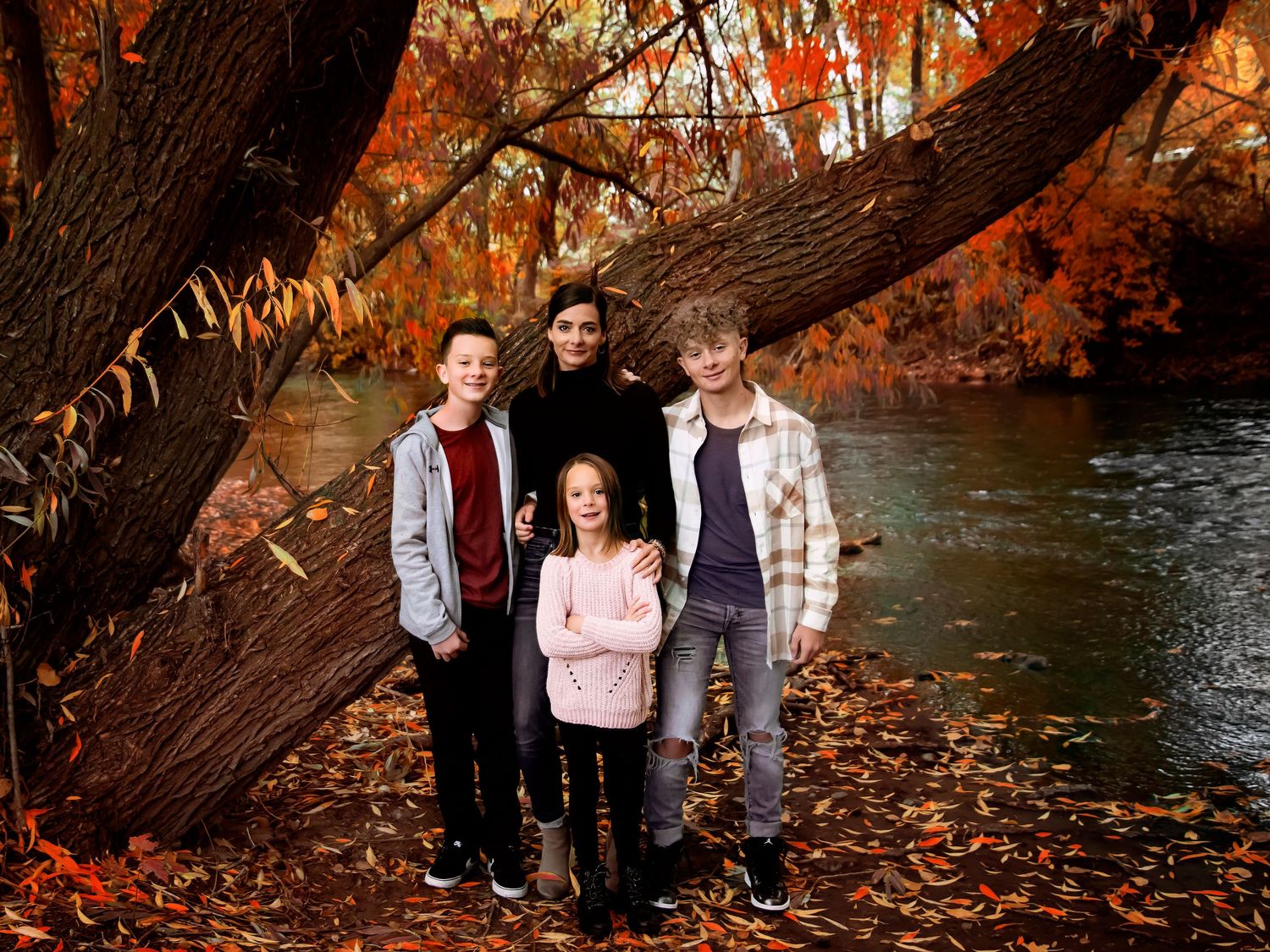Family portrait beneath autumn trees next to a river with red and orange fall colors.