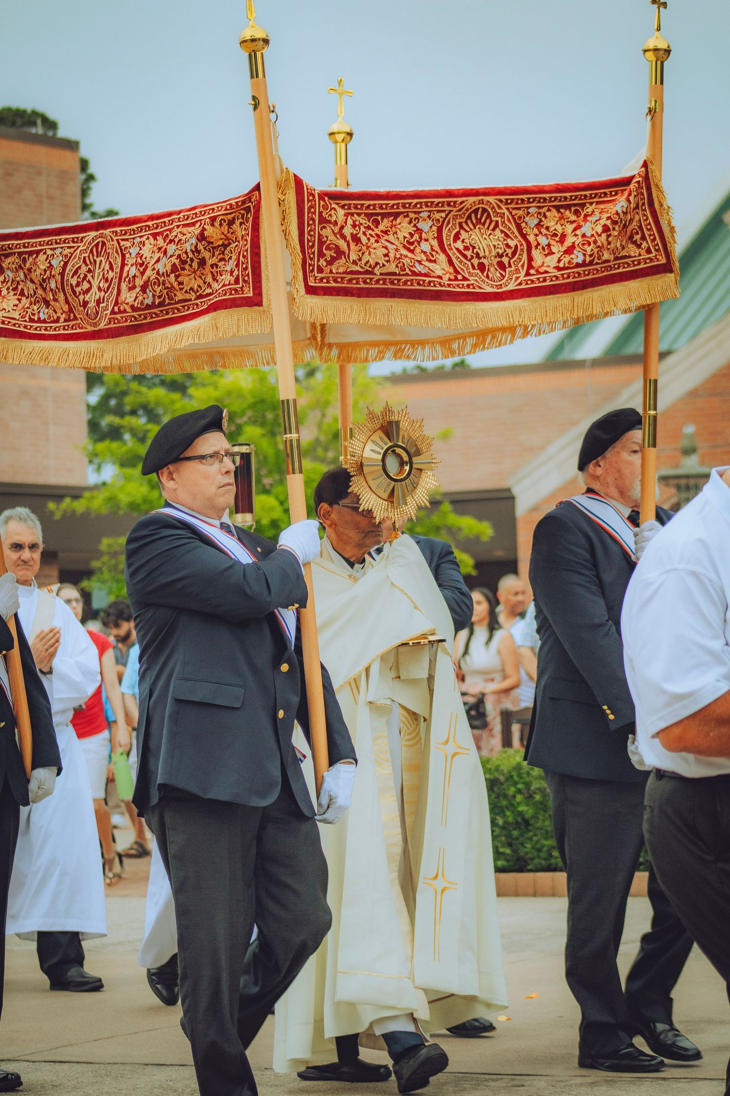 A priest carries a monstrance under a red canopy during a solemn Corpus Christi procession.