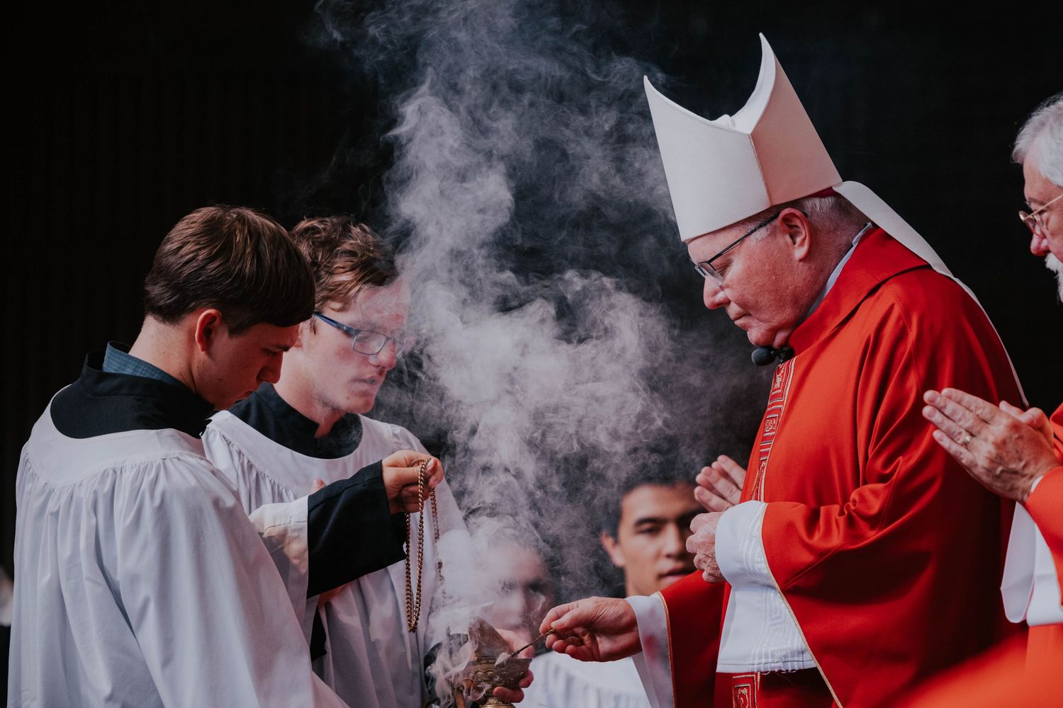Catholic bishop in red vestments performing a religious ceremony with altar servers holding incense during a Mass.