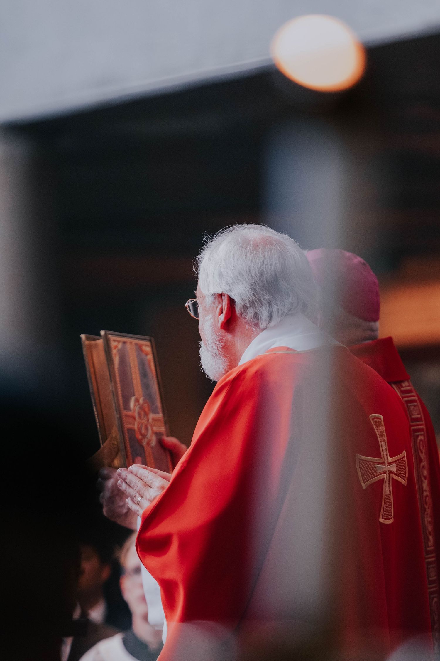 Elderly Catholic bishop in red vestments holding a religious icon during a ceremonial procession.