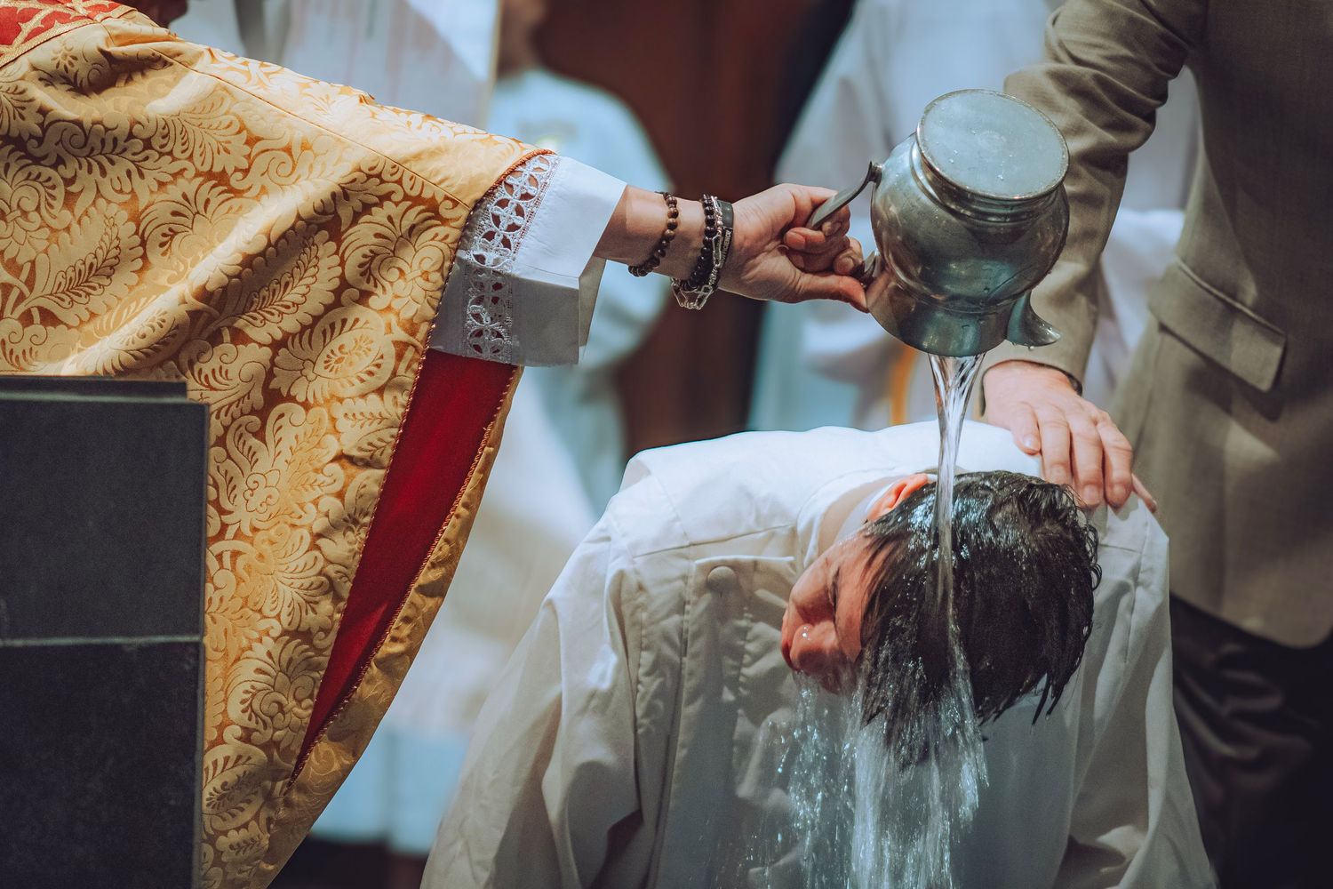 Catholic priest pouring baptismal water over a person's head during a baptism ceremony.