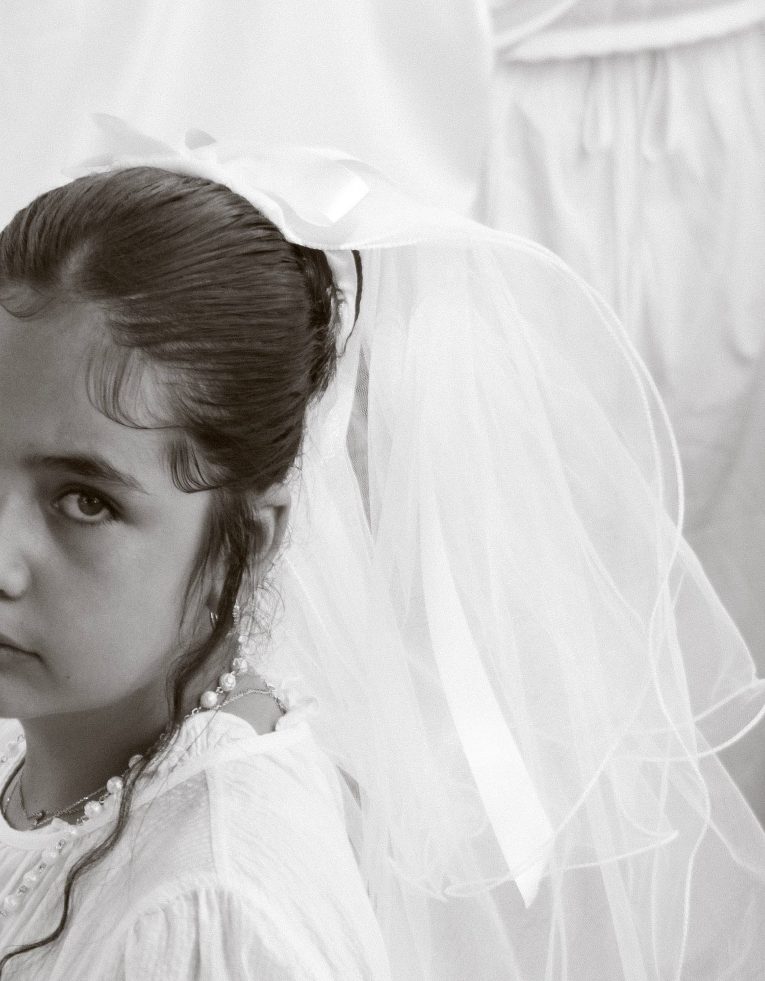 Black and white portrait of a young girl in white veil and dress at her First Communion.