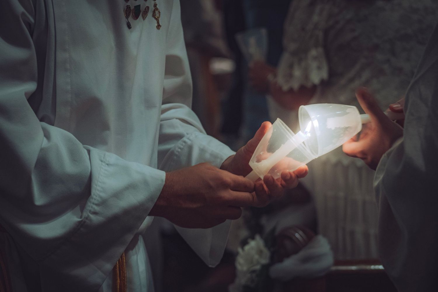 Altar boys in white robes pass a glowing white candle during a Catholic religious ceremony.
