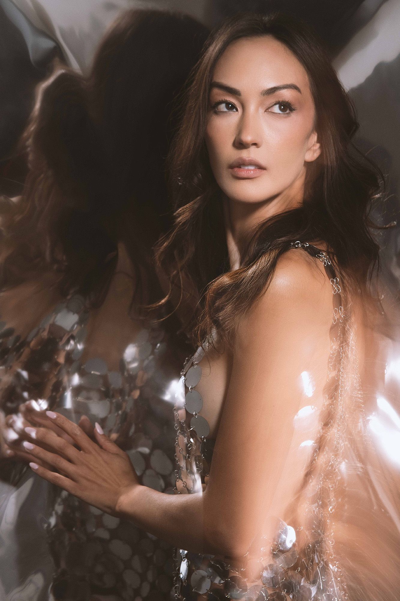 Woman in silver sequin dress posing with reflective metallic background creating dreamy light effects.