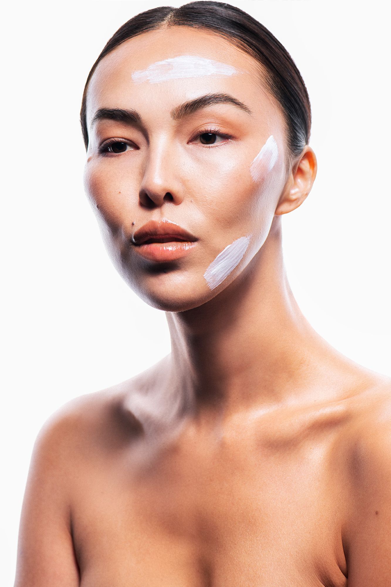 Woman with white cream stripes applied on face and neck for skincare beauty treatment on white background.